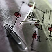 Photograph of paper clips on top of a hand-drawn electrical diagram.
